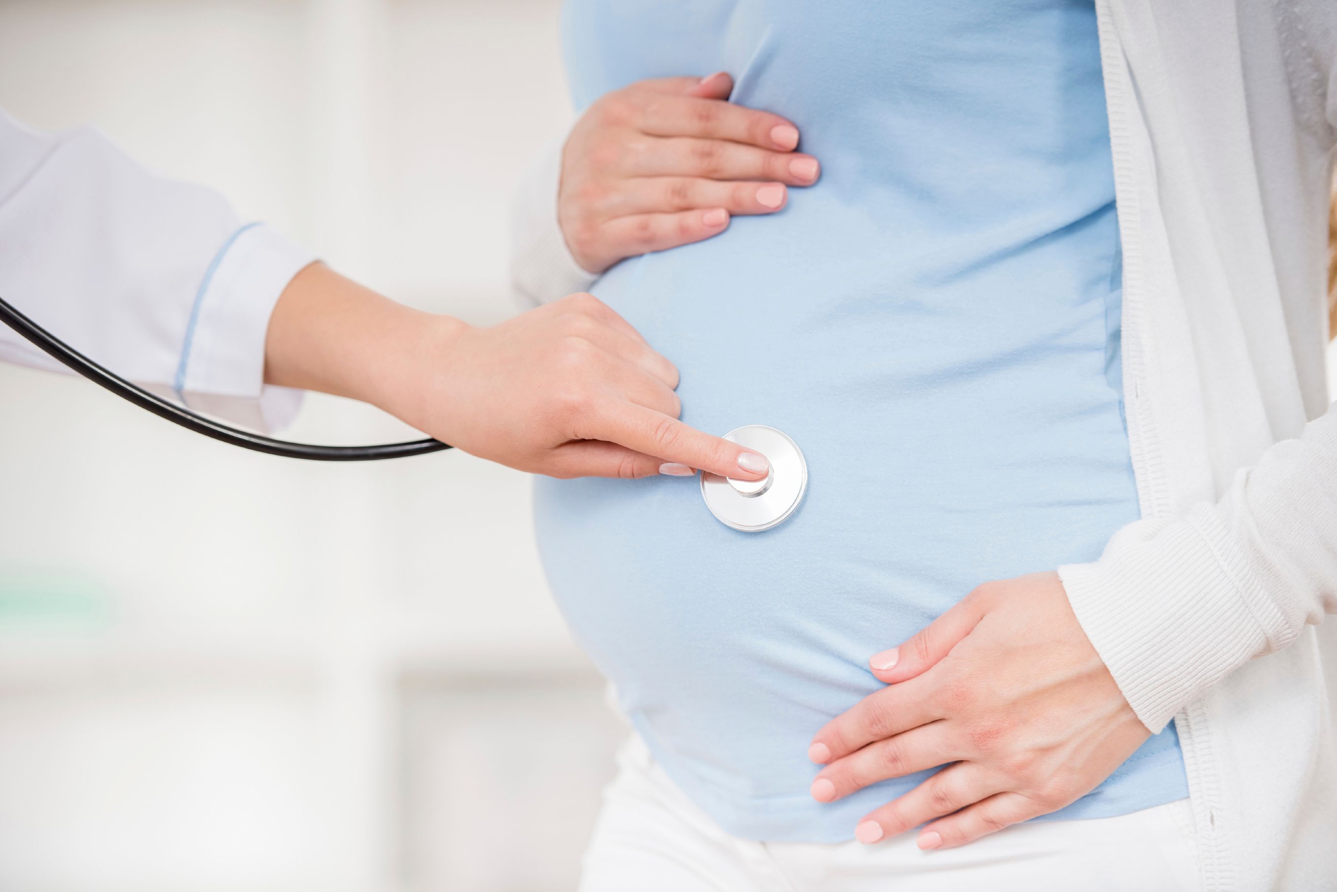 Pregnant woman with doctor placing stethoscope on stomach